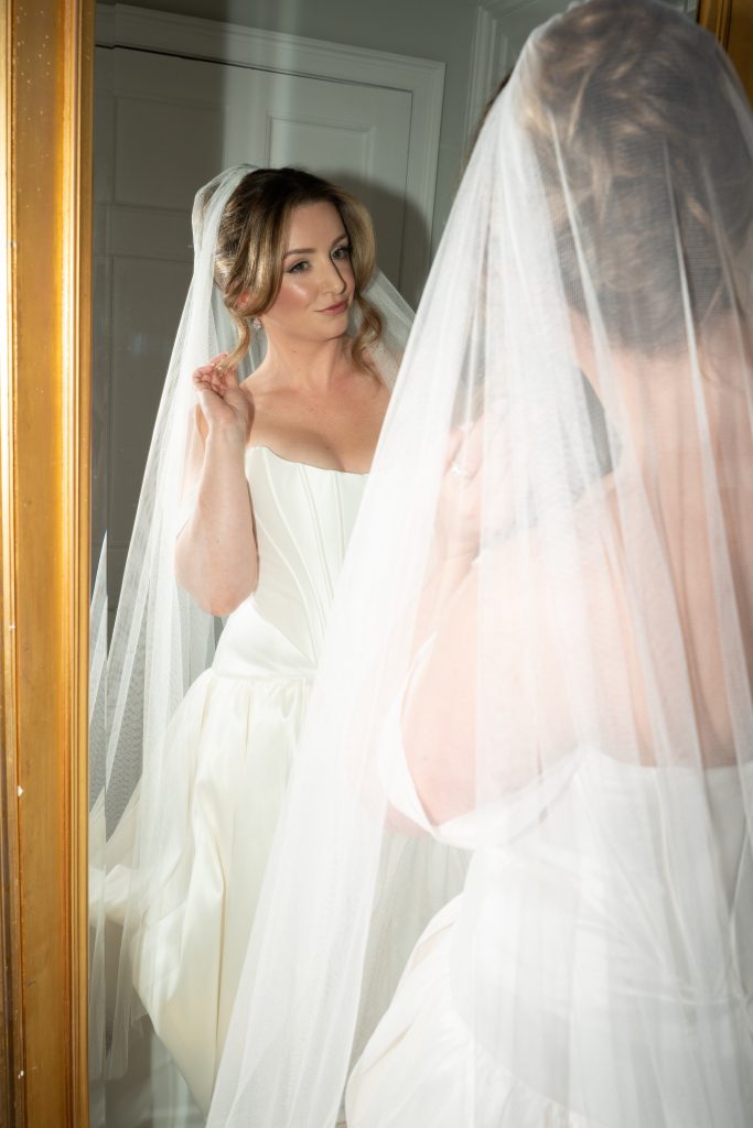 Bride adjusting veil in mirror by Liz Patey